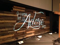 a large wooden sign that reads come let us adore him on the side of a wall