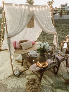 a table with flowers and candles under a canopy on the beach