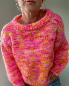 a woman wearing a pink and yellow sweater with her hands on her hips looking at the camera