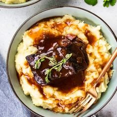 two bowls filled with mashed potatoes covered in gravy and garnished with herbs