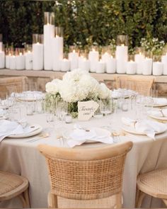 the table is set with white flowers, candles and place cards for guests to sit at