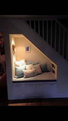 a bed in the corner of a room under a stair case with pillows on it