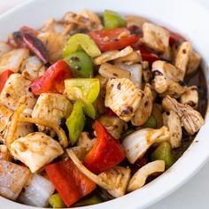 a white bowl filled with chicken, peppers, and onions on top of a table