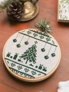 a cross stitch christmas ornament on a wooden table next to a pine cone