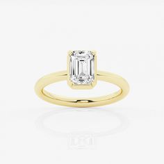 a yellow gold ring with an emerald cut diamond in the center, on a white background