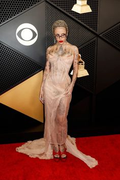 a woman with tattoos on her body standing in front of a red carpet at an awards event