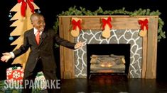 a young boy in a suit and tie standing next to a fireplace with presents on it