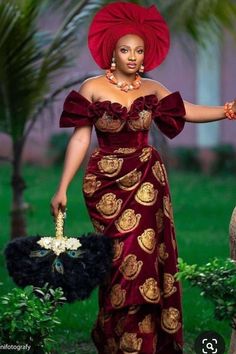 an african woman in a red dress and head wrap holding a black bag with gold designs on it