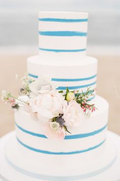 a white and blue wedding cake sitting on top of a table next to the ocean