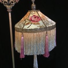 a lamp that has a rose on it and some tassels hanging from it