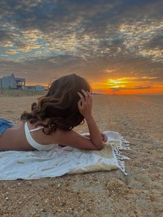 a woman laying on top of a beach next to the ocean under a cloudy sky