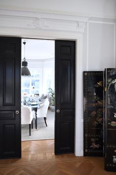 an open door leading to a dining room with black painted doors and chairs in the background