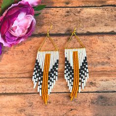 the beaded fringe earrings are hanging from hooks on a wooden table next to flowers