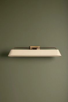 a wall mounted light on the side of a green wall with a gold bar at the top