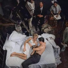 a man and woman laying in bed surrounded by other people