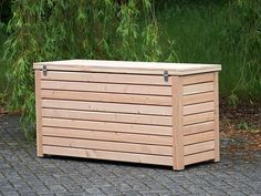 a wooden storage box sitting on top of a gravel road next to a green tree