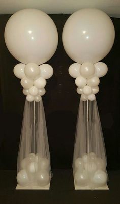 two clear vases with white balloons in them on a black tableclothed surface