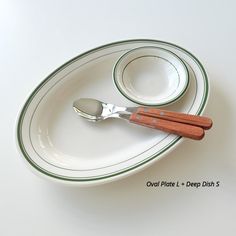 two spoons are sitting on top of a white plate with green trim around it