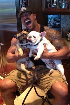 a man holding two small dogs in his arms while sitting on a stool next to a refrigerator