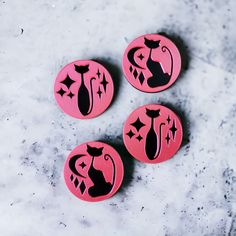 three pink buttons with black designs on them sitting on a marble surface, next to each other