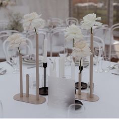 white flowers are in vases on top of a table with silverware and wine glasses