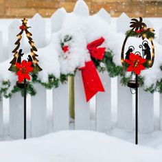 three christmas decorations in the snow near a white picket fence with red bows on it