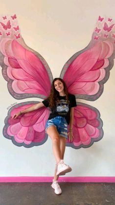 a woman posing in front of a wall with a pink butterfly on it's wings