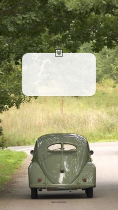 an old green car parked on the side of a road under a tree with a white sign hanging from it's roof