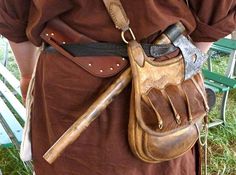 a person wearing a brown outfit holding a leather bag with two large knives in it