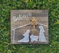 a wooden sign with string art on it that says believe and two dogs in front of the nativity scene