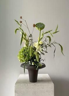 an arrangement of flowers in a black vase on a white pedestal against a gray wall