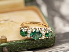 A wonderful statement piece, this vintage ring will elevate your outfits. The ring was made in 1967 and three green stones are the main part. The centre one is bigger than the side ones and they all have a unique dark green colour. In between then, four pearls make their appearance. The sides of the ring have repeated beautiful detail and its shank is a half round. Hallmarks: The ring is stamped 9, 375, and has the letter m for 1967. An engraving of love inside the shank, shows that the ring was Antique Green Ring With 17 Jewels, Heirloom Green Emerald Ring With Three Stones, Heirloom Style Three Stone Green Emerald Ring, Vintage Hallmarked Emerald Jewelry, Vintage Emerald Rings For Wedding, Vintage Oval Three-stone Ring, Vintage Oval Three Stone Ring, Vintage Emerald Rings For May Birthstone, Vintage Emerald Ring With May Birthstone