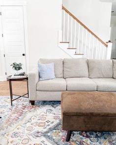 a living room with a couch, ottoman and rug on the floor in front of a stair case