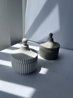 two white dishes sitting next to each other on top of a table in front of a window