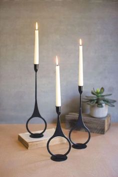 three black candlesticks sitting on top of a wooden table