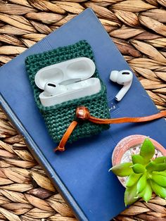 an apple airpods case sitting on top of a book next to a succulent plant