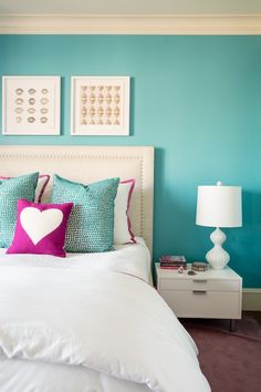 a white bed topped with lots of pillows next to a night stand and two pictures on the wall