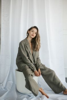 a woman sitting on top of a white toilet in front of a white curtain with her legs crossed