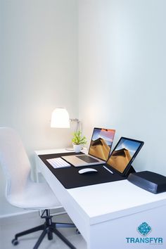 an office desk with two laptops sitting on top of it next to a lamp