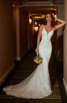 a woman in a white wedding dress standing next to a wall and holding a bouquet