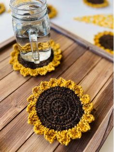 two crocheted coasters sitting on top of a wooden table next to a jar of water