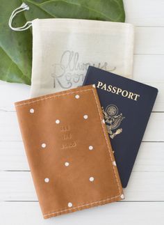 two passport cases sitting next to each other on top of a white wooden table with a green leaf