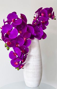 a white vase filled with purple flowers on top of a table