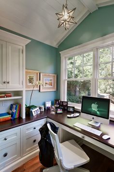 a desk with a computer on top of it in front of a window and bookshelf