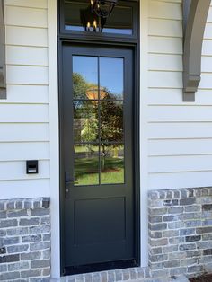 a black front door on a white house with brick pillars and an arched glass window