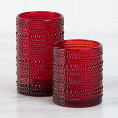 two red glass vases sitting on top of a white counter next to each other