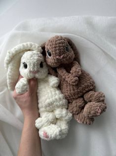 someone is holding two stuffed animals in their hands on a white sheet with the covers pulled back