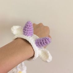 a crocheted bunny wristband is shown on someone's arm, wearing a purple and white hat