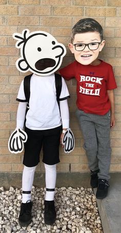 two young boys standing next to each other in front of a brick wall wearing costumes