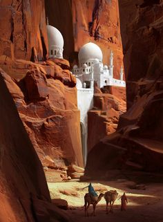 two camels are walking through the desert with some buildings in the background and people on horseback